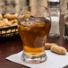a glass of liquid with ice and a peanuts in the background