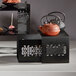 A black metal Rosseto Mosaic nesting riser set with a teapot and small plates on a table.