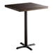 A Lancaster Table & Seating square bar height table with a wood top and cast iron base.