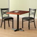 A Lancaster Table & Seating wood table with mahogany finish and a cast iron base plate with two chairs.