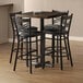 A Lancaster Table & Seating butcher block bar table with black chairs around it.