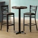 A Lancaster Table & Seating round wood table with two black chairs on a cast iron base.