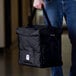 A man holding a black Cambro insulated food delivery bag with a handle.