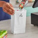 A hand putting candy in a white Duro paper bag.