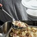 A person using a Vollrath black stainless steel Spoodle to serve food from a bowl.