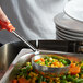 A person using a Vollrath orange stainless steel spoodle to serve mixed vegetables.