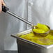 A person using a Vollrath black perforated portion spoon to scoop food from a container.