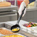 A person holding a black Vollrath High Heat Solid Round Nylon Spoodle over a tray of macaroni and cheese.