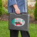 A person holding a black case with a red Choice portable stove inside.