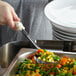 A hand using a Vollrath Ivory Perforated Spoodle to serve vegetables.