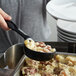 A person using a black Vollrath spoodle to serve food from a bowl.