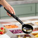 A hand holding a black Vollrath Spoodle over a bowl of vegetables on a salad bar counter.