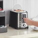 A person using a Hamilton Beach 2 slice bagel toaster in a hotel room kitchen.