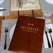 A table set with H. Risch Smokey Quartz woven vinyl placemats, a menu, and a glass of water.