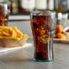 A jade plastic GET soda glass filled with cola and ice on a table with a bowl of fries.