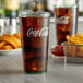 A jade plastic tumbler filled with Coca-Cola and ice sitting on a table with a plate of fries.