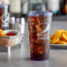 A blue Pepsi tumbler filled with soda and ice on a table with a plate of fries.