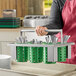 A woman holding a Steril-Sil stainless steel flatware basket with lime green plastic cylinders filled with utensils.