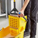 A person using a Lavex yellow mop bucket side press wringer to clean a mop.