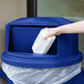 a hand holding a white container in a blue trash can