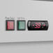 A digital clock and power switch on a wall above a white Avantco glass door merchandiser.