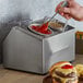 A person pouring sauce into a Steril-Sil condiment container on a counter.