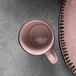 A Libbey pink stoneware mug next to a pink plate on a grey surface.