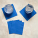 A set of cobalt blue square beverage or cocktail napkins, with two glasses of ice water placed on two of the napkins.