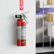 A red Buckeye 2.5 lb. Halotron fire extinguisher with a fixed nozzle and DOT vehicle bracket mounted on a wall.