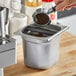 A hand knocking ground coffee into a silver container with the Choice 6" Deep Espresso Knock Box.