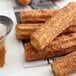 A sieve sprinkling Regal Ground Cinnamon on a pile of churros.