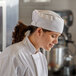 A woman in a white chef's uniform wearing a white mesh Choice chef hat.