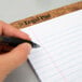 A hand using a pen to write on a TOPS wide ruled legal pad.