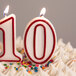 A close up of a white cake with a red and white outlined number 0 candle.