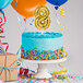 A white birthday cake with a gold number 8 balloon on top.