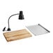 A carving station kit with a black heat lamp, a wooden cutting board, and a metal drip pan.