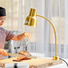 A woman cutting a piece of meat on a wooden cutting board with an Avantco gold heat lamp overhead.