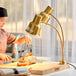 A woman using a knife to cut meat on a wooden cutting board under a gold heat lamp.