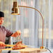 A woman cutting cooked meat on a cutting board with an Avantco gold flexible heat lamp above her.