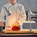 An Avantco chef in a chef's uniform cutting a piece of meat on a cutting board.