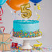 A close up of a white birthday cake with a gold "5" balloon topper.