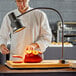 An Avantco carving station with a chef in a white coat cutting a ham on a cutting board.