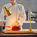 An Avantco chef in a white coat uses a carving station to cut ham on a cutting board.