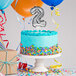 A white birthday cake with a silver "2" balloon on top.