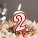 A red and white outlined number two birthday candle on a cake.