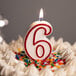 A white cake with a red outlined number six candle on top.