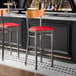 Two Lancaster Table & Seating Boomerang clear coat finish bar stools with red vinyl seats and cherry wood backs at a bar counter.