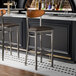 Two Lancaster Table & Seating Boomerang bar stools with dark brown vinyl seats at a wood bar.