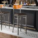 Two Lancaster Table & Seating Boomerang bar stools with dark brown vinyl seats at a bar counter.