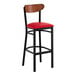 A bar stool with a black metal frame, red vinyl seat, and an antique walnut wood backrest.
